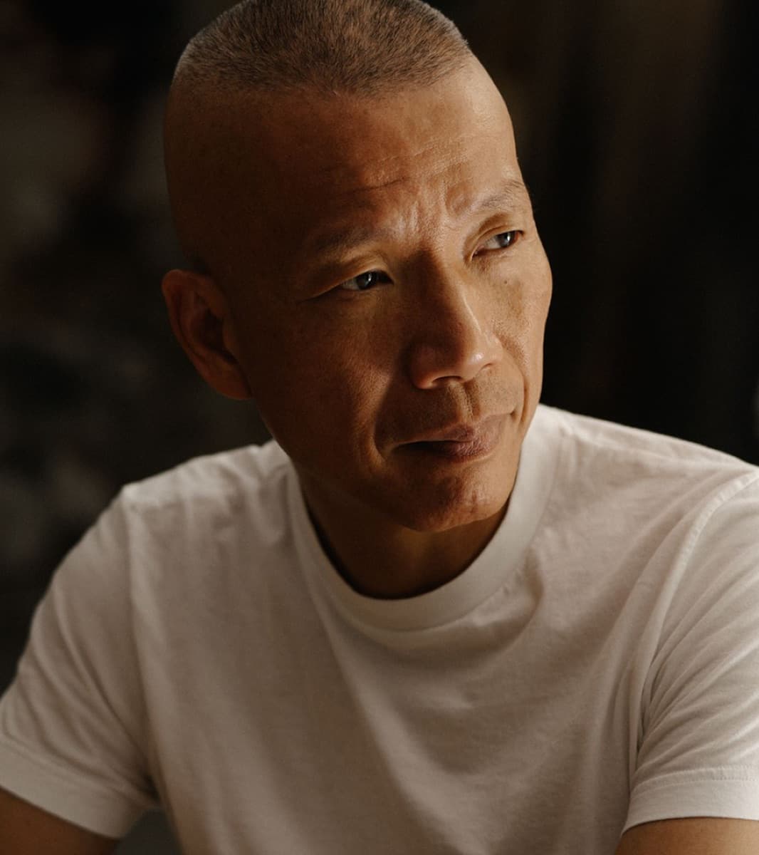A man with close-cropped hair in a white T-shirt, looking off to the side